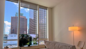 Une chambre moderne dotée d’une grande fenêtre, d’un téléviseur à écran plat, d’un canapé blanc et d’un lampadaire.