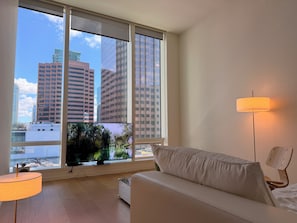 A modern room with a large window, a flat-screen TV, a white sofa, and a floor lamp.