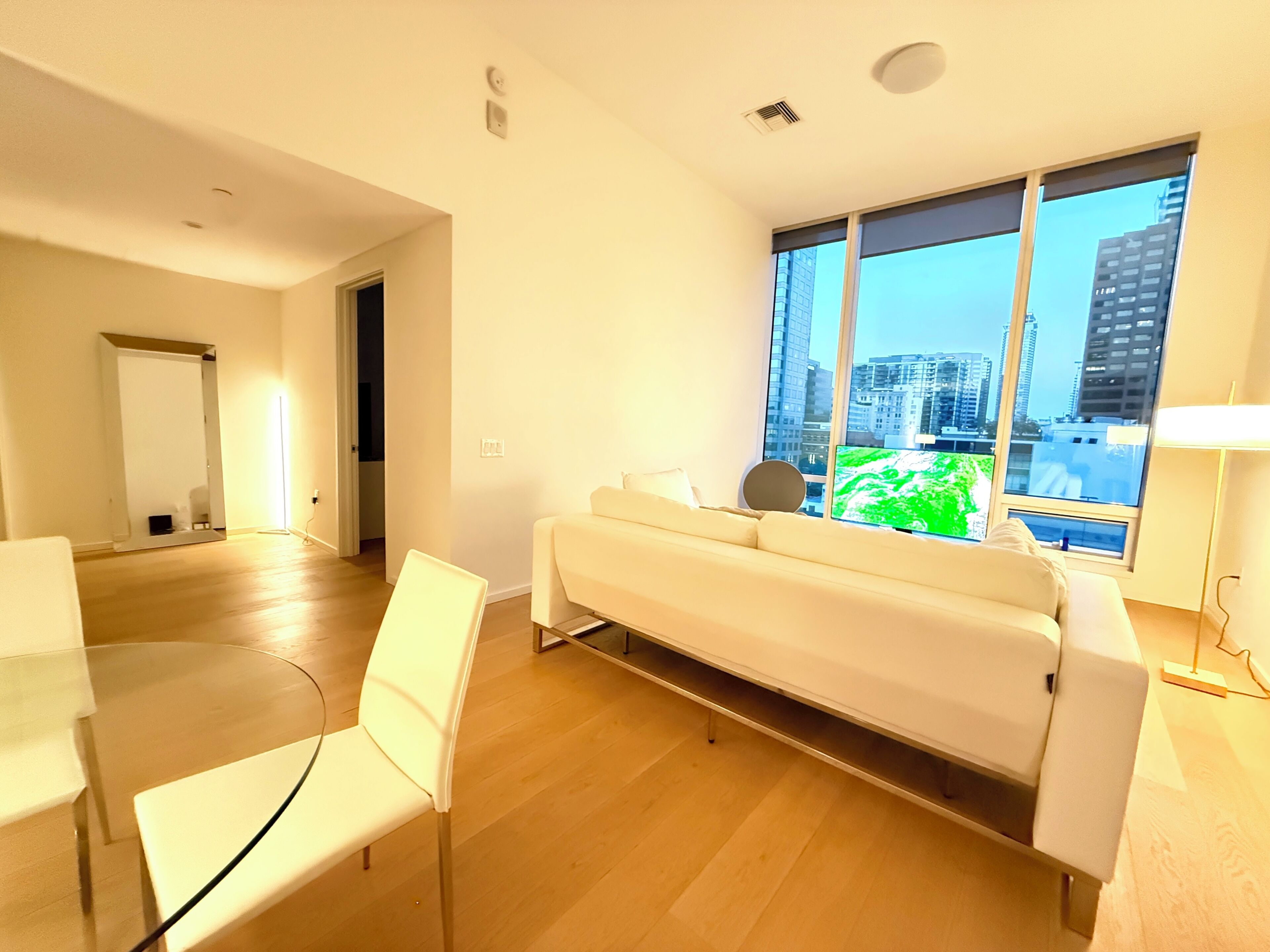 A modern living room with a sofa, chairs, a TV, and a large window with a city view.