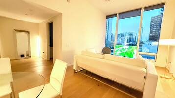 A modern living room with a sofa, chairs, a TV, and a large window with a city view.