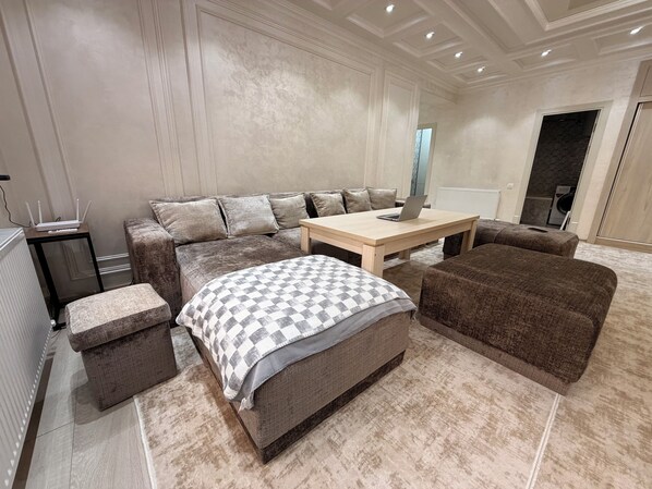 A modern bedroom with a large bed, a sofa, a coffee table, and a small table with a laptop.