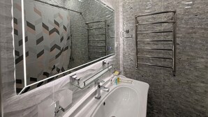 Un baño moderno con un espejo grande, estante de vidrio, bañera y perchero.