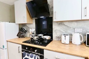 A compact kitchen with a stove, toaster, kettle, and a microwave.