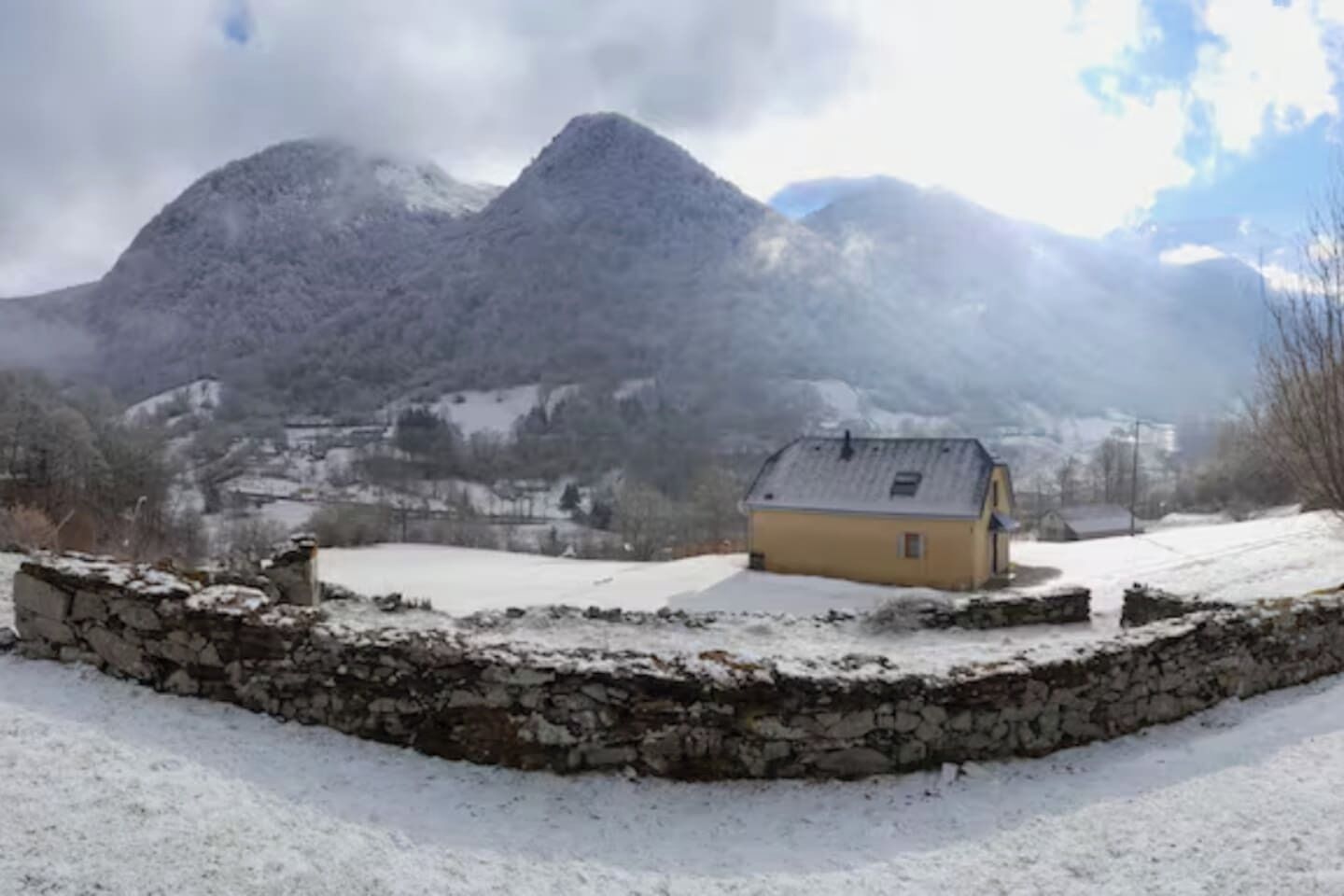 A snow-covered landscape with a stone wall and a yellow building.