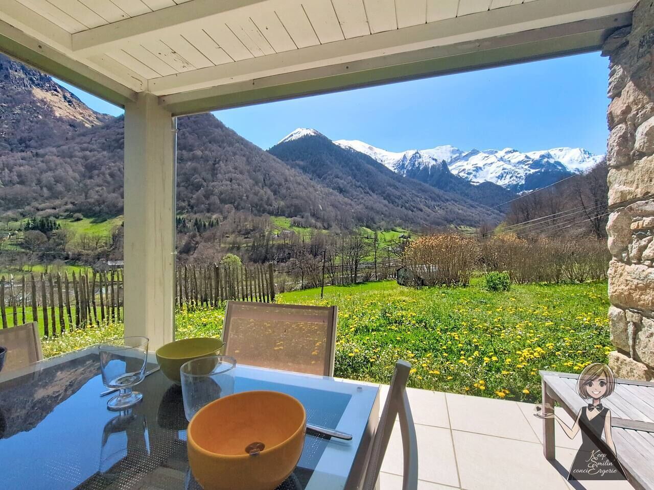 A table with a glass, a bowl, and a chair in a covered outdoor area with a mountain view.
