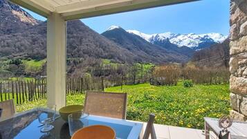 A table with a glass, a bowl, and a chair in a covered outdoor area with a mountain view.