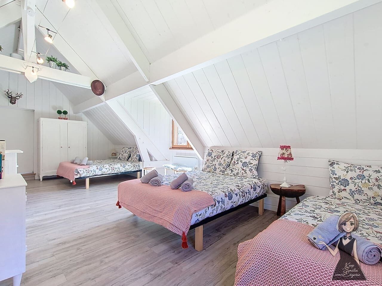 A loft bedroom with two beds, a white wardrobe, and a small table with a lamp.