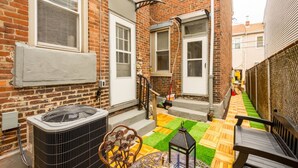 A brick building with a patio area featuring a wooden bench, a metal chair with a rose design, and a lantern. - Double Living, Patio BBQ, Massage & South Side Fun (Pittsburgh)