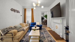 A living room with a sofa, a blue armchair, a coffee table, a fireplace, and a TV mounted on the wall. - Double Living, Patio BBQ, Massage & South Side Fun (Pittsburgh)