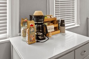 Ein Kaffee-Bereich mit Kaffeemaschine, einer Kaffeetütenpackung, einem Glasbehälter, einer Holzkiste und einer Stapel Tassen.