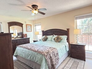 Ein Schlafzimmer mit Bett, Deckenventilator, Kommode, Nachttisch und Fenster.