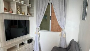 A living room with a flat-screen TV, a grey sofa, a wooden cabinet, and a window with curtains. - Spacious 3-bedroom apartment in perfect Barranquilla with AC (Barranquilla)