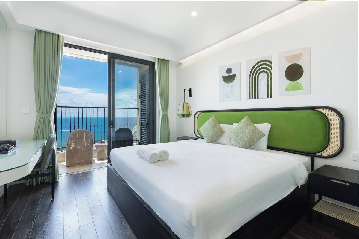 Habitación de hotel con cama, escritorio, silla, balcón con vistas y obras de arte en la pared.