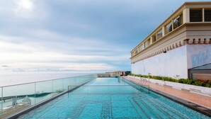 Ein Dachpool mit Infinity-Kante, klarem blauen Wasser, einer Glasbrüstung und Blick auf das Meer.