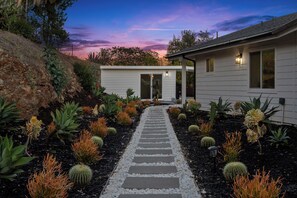 Ein Weg führt zu einem Haus mit einem Garten, der Kakteen und Sukkulenten beherbergt.