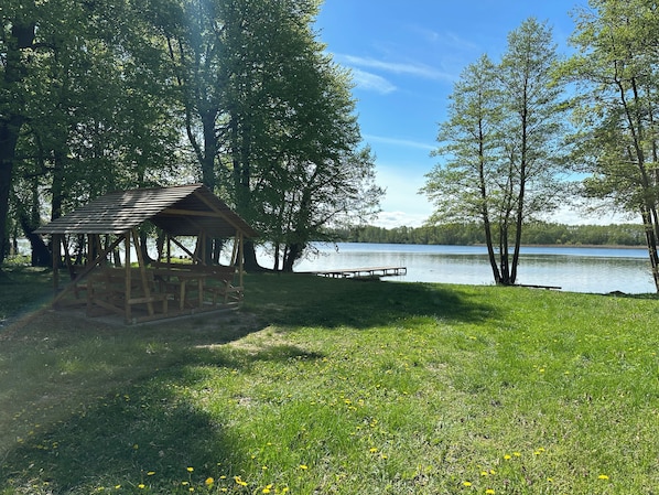 A wooden gazebo with benches, a dock extending into a lake, surrounded by trees. - Idyllic location - vacation home for families with dogs 1 hour from Berlin on the lake. (Neuruppin)