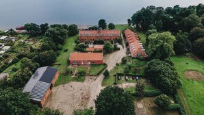 Oversigtsbillede af et stort bygningskompleks med flere bygninger, omgivet af grønt og en sø.