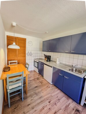 A compact kitchen with wooden cabinets, a built-in oven, a dishwasher, and a dining area with a wooden table and chairs. - Idyllic location - vacation home for families with dogs 1 hour from Berlin on the lake. (Neuruppin)