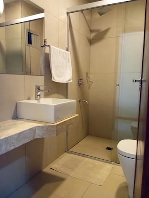 Een badkamer met een douchecabine van glas, een witte wastafel en een toilet.