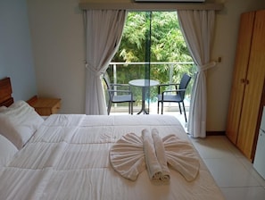 Een hotelkamer met een bed, een balkon met stoelen en uitzicht op groen.