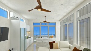 Una cocina moderna con vista a la playa, un comedor con una mesa blanca y una sala de estar con un sofá blanco.