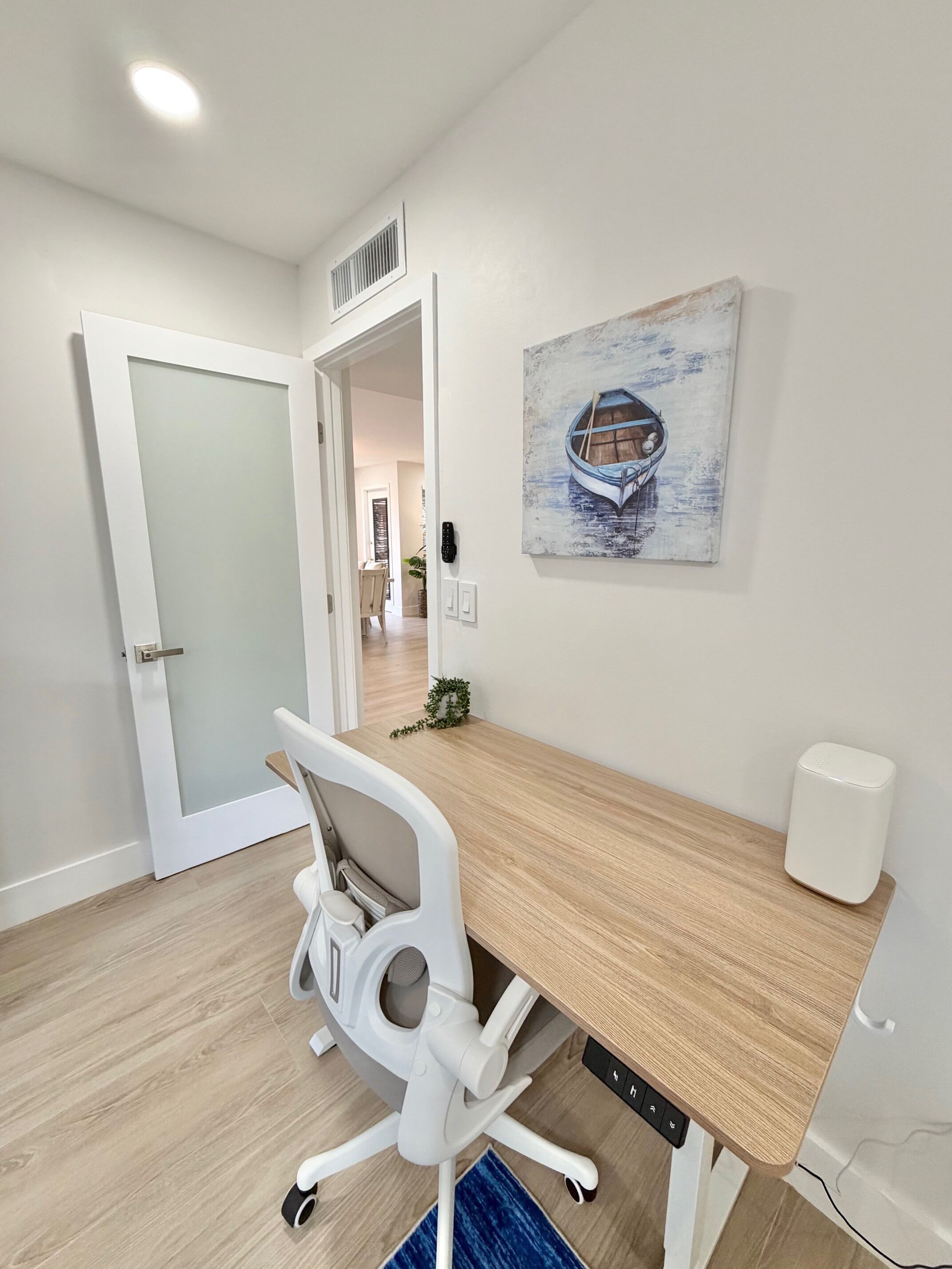 Een moderne kantoorruimte met een houten bureau, een witte bureaustoel en een schilderij van een boot aan de muur.