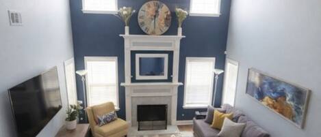 A living room with a fireplace, sofa, TV, and ceiling fan.