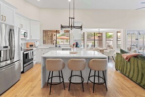 A modern kitchen with white cabinetry, stainless steel appliances, and a central island with bar stools. - The Ultimate Stay & Play Retreat • 4BR • Sleeps 13 (Chandler)