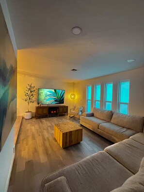 A living room with a large flat-screen TV, a wooden coffee table, a beige sofa, and a potted plant. - Tropical Getaway (Lehigh Acres)