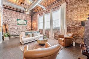 A cozy living room with a brick wall, a sofa, a coffee table, and a leather chair. - Historic Loft in Grant Park 3 less than 3 minute walk to MARTA Rail (Atlanta)