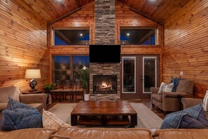 A log cabin interior with a fireplace, wooden walls, a television, and a cozy seating area.
