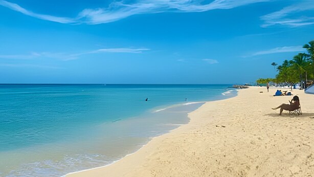 Une plage avec une eau d’un bleu limpide, un rivage sablonneux et quelques personnes.