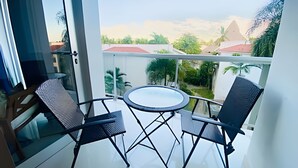 Un balcon avec deux chaises et une table, donnant sur un quartier résidentiel avec des maisons et de la verdure.