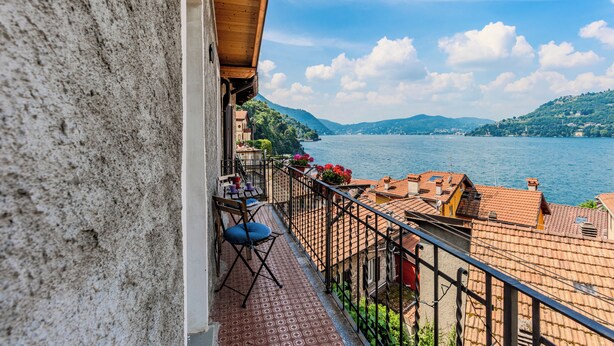 Un balcon donnant sur un lac et des collines, une table avec des chaises et une balustrade.