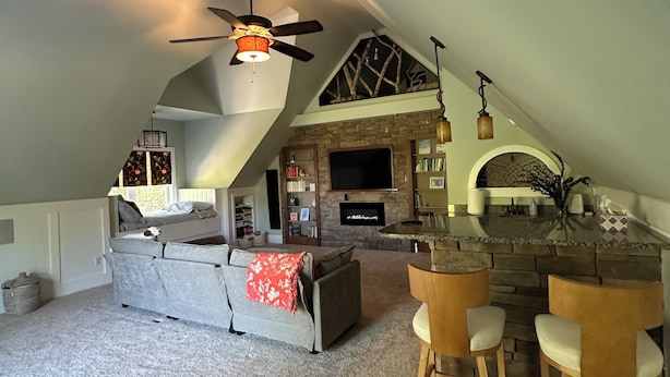 A loft-style living space with a high ceiling, a fireplace, a television, and a dining area with bar stools.