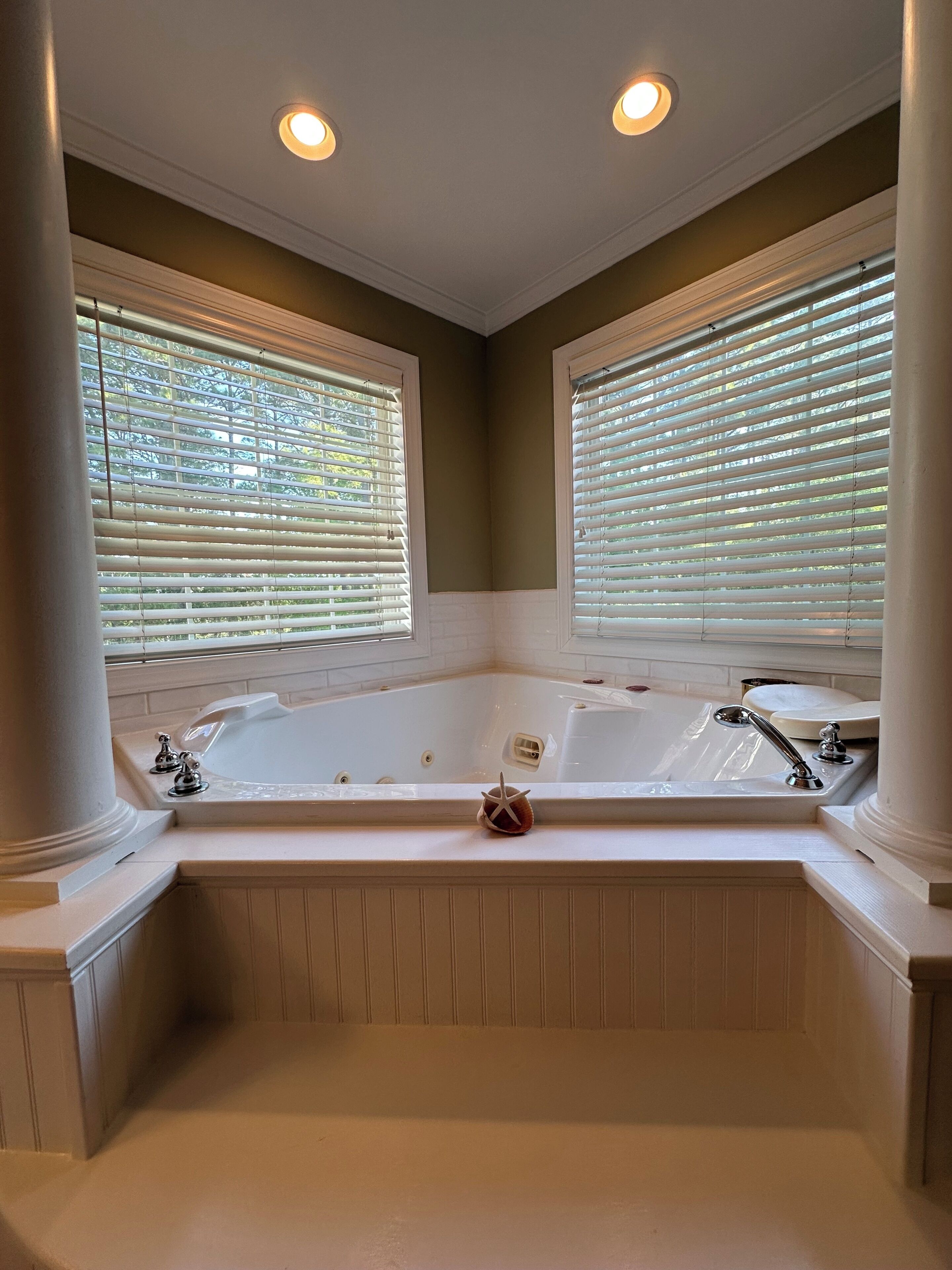 A bathroom with a large bathtub, two windows with blinds, and a starfish decoration.