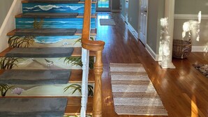 A staircase with a painted ocean scene, wooden handrails, and a hallway with a wooden floor and a basket.