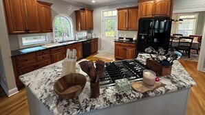 A kitchen with wooden cabinets, a black refrigerator, a marble countertop, and a dining area with a table and chairs.