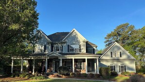 A two-story house with a porch, brick foundation, and a large lawn.