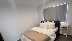 Un dormitorio con cama, mesita de noche, lámpara y ventana con persianas.