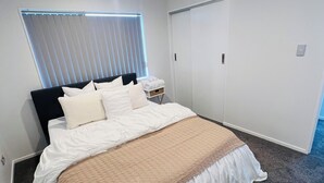 Un dormitorio con cama, mesita de noche, ventana con persianas y puerta.