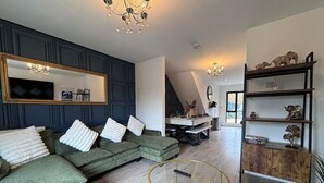 Ein modernes Wohnzimmer mit einer Eckcouch, einem Glastisch, einer Holzkommode und einer Deckenleuchte.