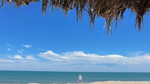 Vista de la playa con una silla de descanso, una mesita y una persona caminando hacia el mar.
