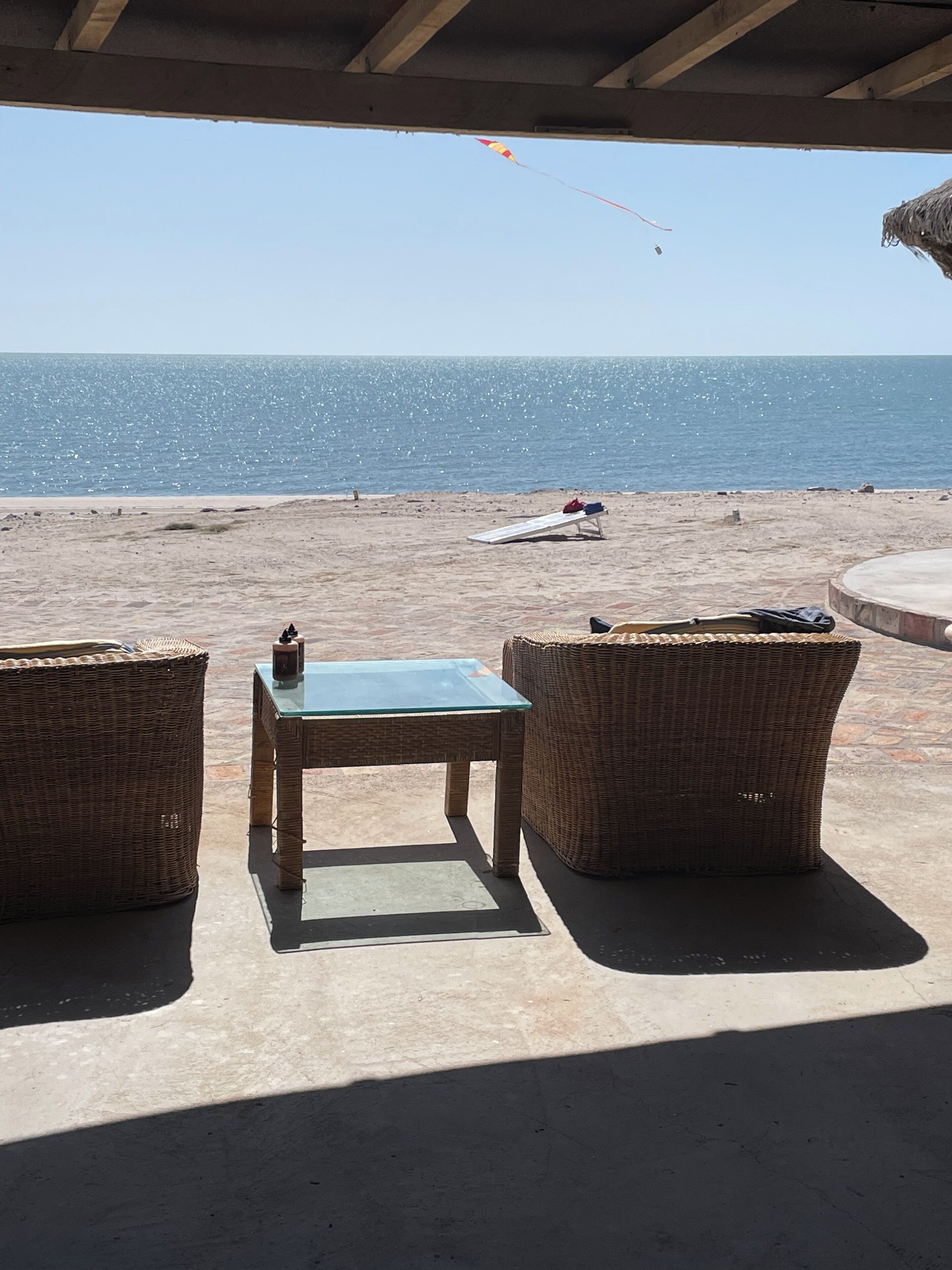 Een zitgedeelte aan het strand met rieten meubels en een glazen tafel, met uitzicht op de oceaan.