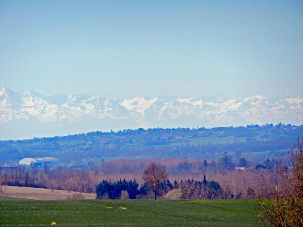 A mountainous landscape with snow-capped peaks in the distance, a green field in the foreground, and a clear sky.