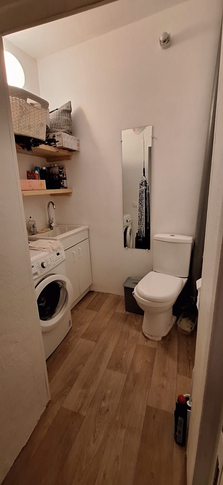 Une petite salle de bain équipée d’un lave-linge, de toilettes et d’un miroir qui reflète le paysage urbain.
