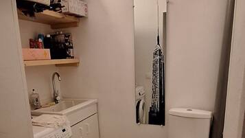 Une petite salle de bain équipée d’un lave-linge, de toilettes et d’un miroir qui reflète le paysage urbain.