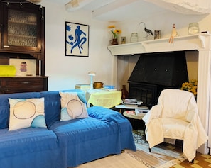 Una sala de estar acogedora con un sofá azul, un sillón blanco, una chimenea y varios objetos decorativos.