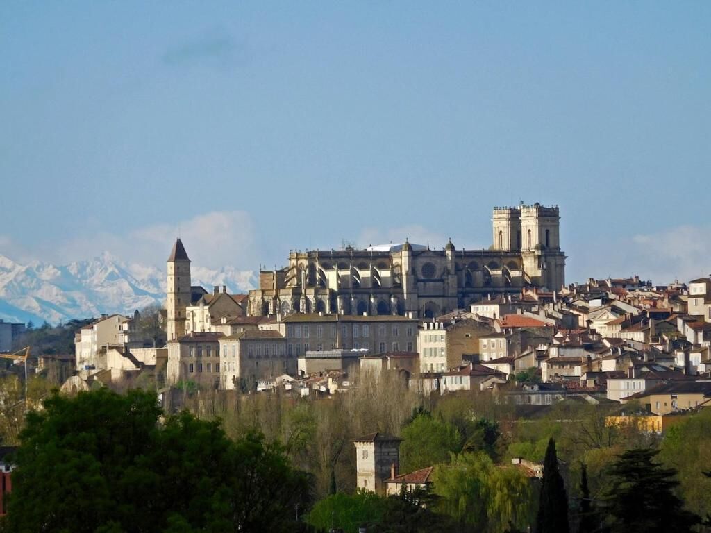 Ville historique dotée d’un imposant édifice qui ressemble à un château, entourée de bâtiments résidentiels et bordée par un paysage montagneux.