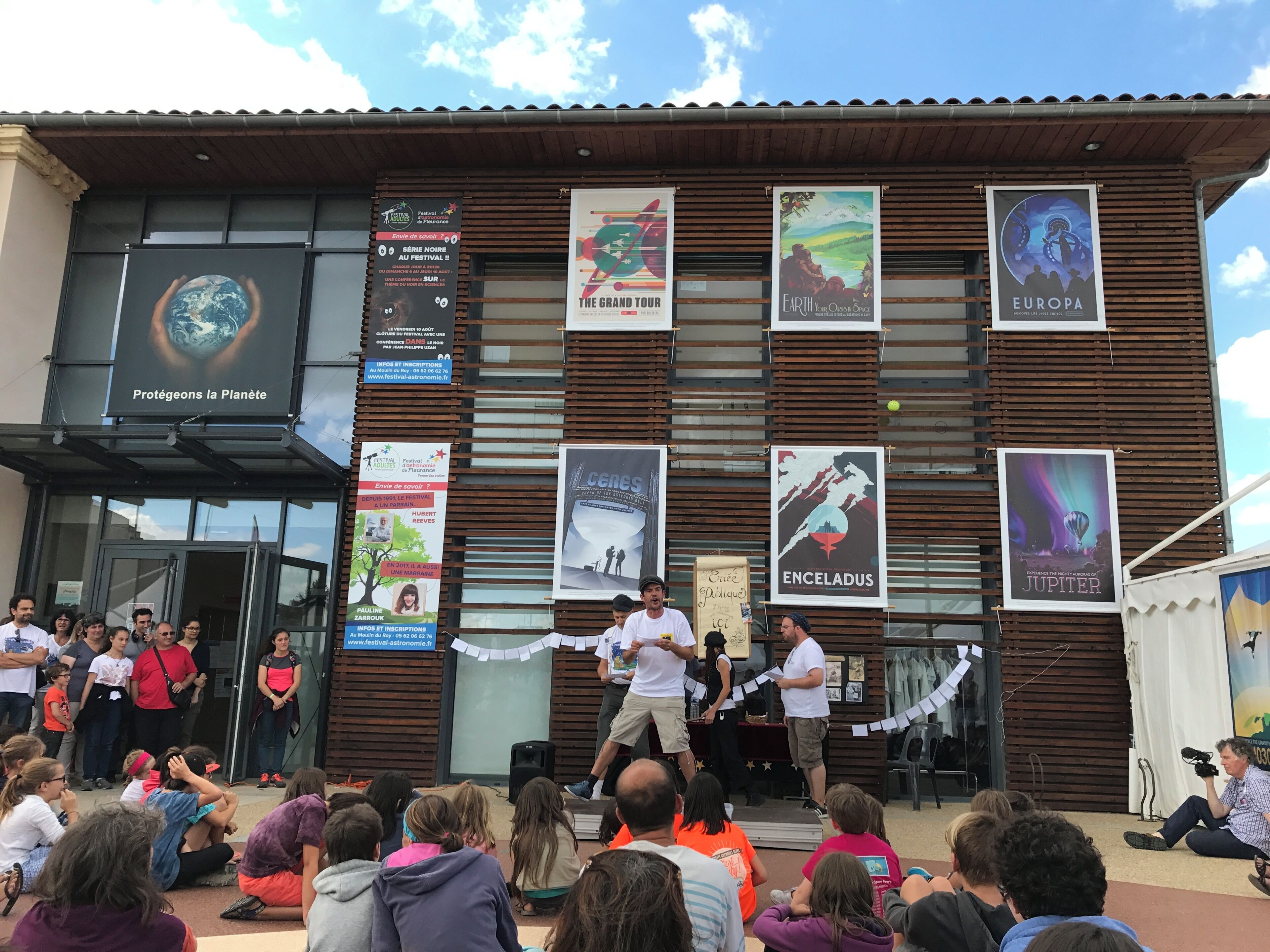 A building with a stage for an event, banners with various themes, and a crowd of people.